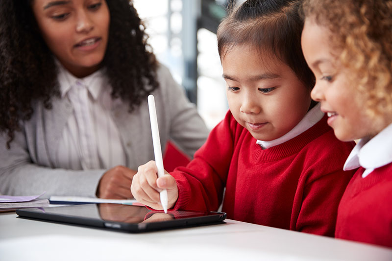 Two girls working on a tablet with their teacher