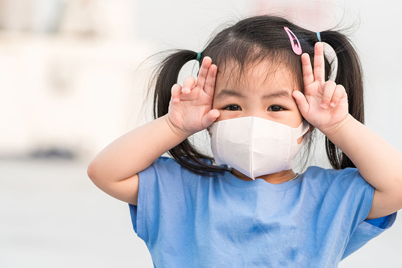 Girl in Pigtails wearing a covid mask and putting her fingers up on her head like bunny ears