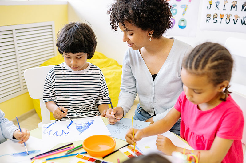 Two girls working on a tablet with their teacher